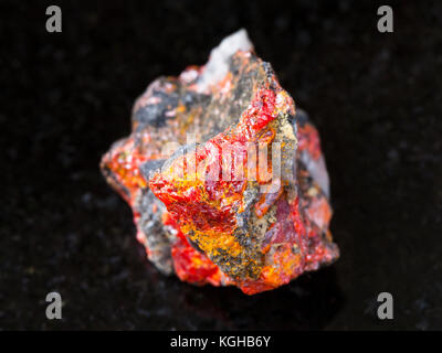 macro shooting of natural mineral rock specimen - rough Realgar crystals on stone on dark granite background from Luhumi mine, Georgia Stock Photo