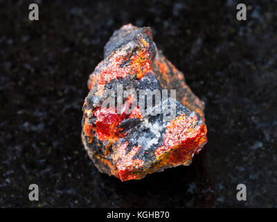 macro shooting of natural mineral rock specimen - raw Realgar stone on dark granite background from Luhumi mine, Georgia Stock Photo