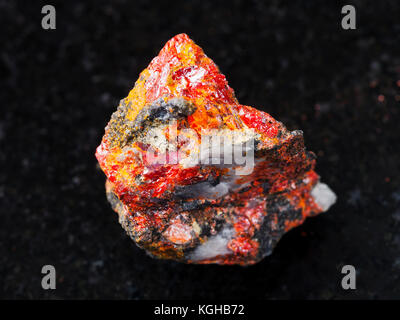 macro shooting of natural mineral rock specimen - rough Realgar stone on dark granite background from Luhumi mine, Georgia Stock Photo