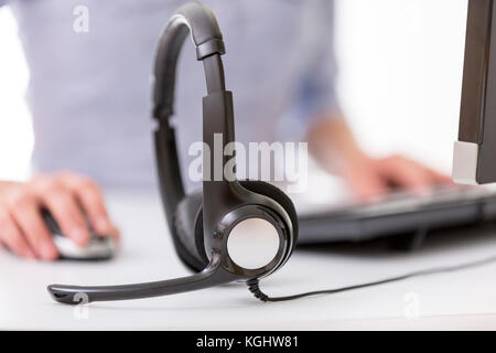 Office desk with headset, female agent and pc on background. Call center support concept Stock Photo