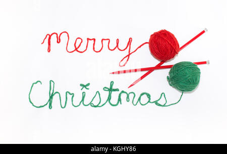 Merry Christmas written in cursive with red and green yarn and photographed from above against a white background. The knitting needles and red and gr Stock Photo