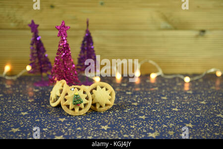 Christmas food photography image of traditional English mince pies with iced tree on top and glitter tree decorations and fairy lights in background Stock Photo
