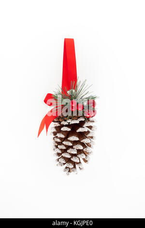 Large hanging pine cone decorated with glitter, red holly berries, fir, ribbon and a bell on white background with lots of copy space. Christmas ornam Stock Photo
