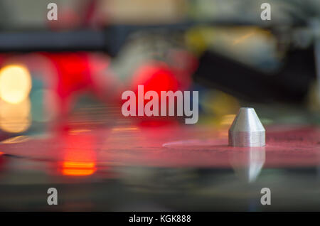 A turntable playing music vinyl record.  Focused on tonearm, needle, platter, vinyl record.  Colorful lights blurred in background with reflections Stock Photo