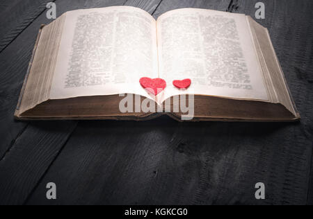 Antique open book with two red hearts on its pages, sitting on a black wooden background. A concept for the love of reading, learning, education or as Stock Photo