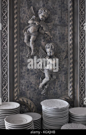 Stack of plates on the showcase with angels on the background. Restaurant utensils with shallow focus. Stock Photo