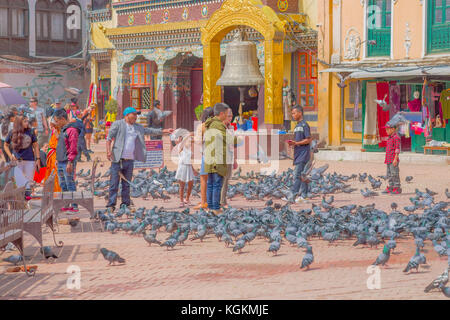 KATHMANDU, NEPAL OCTOBER 15, 2017: Unidentified people walking in the square surrounding of hundred of pigeons in front of a huge bell under a stoned gold structure in Kathmandu Boudhanath Stupa in Boudha town, Nepal Stock Photo