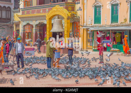 KATHMANDU, NEPAL OCTOBER 15, 2017: Unidentified people walking in the square surrounding of hundred of pigeons in front of a huge bell under a stoned gold structure in Kathmandu Boudhanath Stupa in Boudha town, Nepal Stock Photo