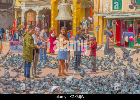 KATHMANDU, NEPAL OCTOBER 15, 2017: Unidentified people walking in the square surrounding of hundred of pigeons in front of a huge bell under a stoned gold structure in Kathmandu Boudhanath Stupa in Boudha town, Nepal Stock Photo