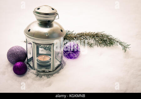 silver lantern with candlelight and silver and purple baubles against snowy background Stock Photo
