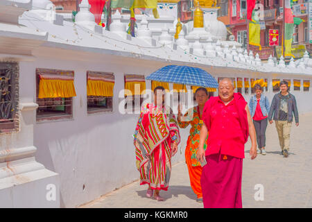 KATHMANDU, NEPAL OCTOBER 15, 2017: Close up of unidentified women walking at outdoors and protecting from the sun using the umbrella, and happy monk walking and wearing typical clothes, close to the monument Boudhanath stupa in Kathmandu, Nepal Stock Photo
