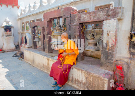 KATHMANDU, NEPAL OCTOBER 15, 2017: Close up of unidentified man sitting at outdoors and holdig in one hand prayer beads and touching a huge bell with his other hand close to the monument Boudhanath stupa in Kathmandu, Nepal Stock Photo