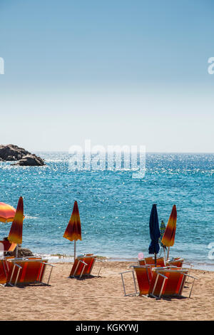 Closed parasols with deck chairs at beach against clear blue sky on sunny day Stock Photo