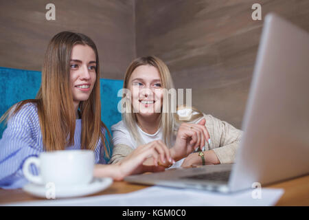 Young female friends using laptop while sitting in restaurant Stock Photo