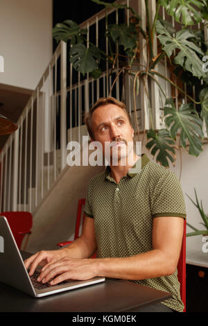 Thoughtful mid adult man looking away while using laptop at table Stock Photo