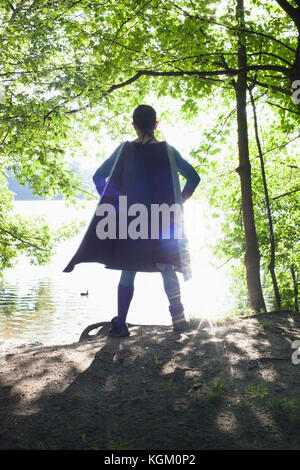 Rear view of superhero standing at riverbank on sunny day Stock Photo