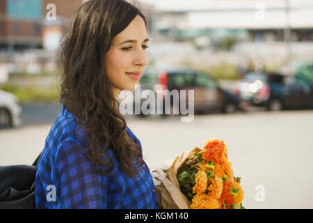 Thoughtful woman holding flowers bouquet in city Stock Photo