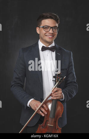 Portrait of smiling young man holding violin while standing against black background Stock Photo