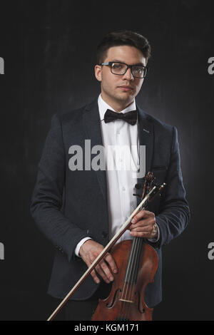 Portrait of confident young man holding violin while standing against black background Stock Photo