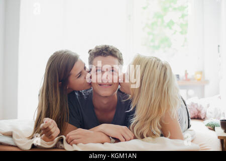 Young female friends kissing handsome man lying on bed at home Stock Photo