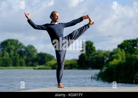Mature man practicing yoga on pier by lake against sky Stock Photo