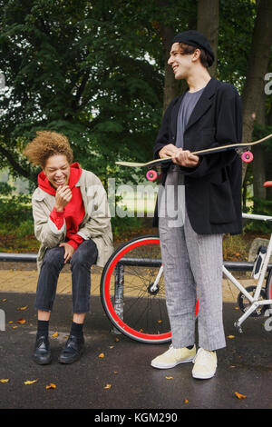 Happy friends with bicycle and skateboard at park Stock Photo