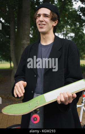 Happy young man holding skateboard while standing at park Stock Photo