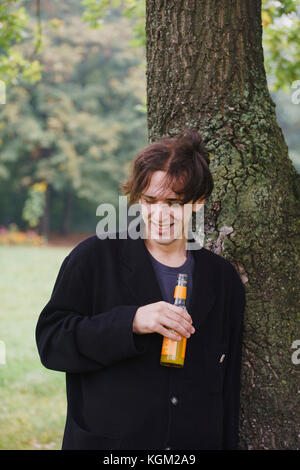 Young man drinking juice while standing by tree Stock Photo