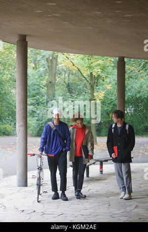 Happy friends talking while walking in gazebo against trees at park Stock Photo