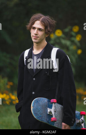 Thoughtful young man carrying skateboard while standing at park Stock Photo