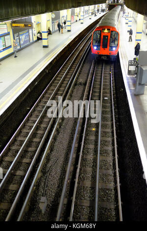 An underground train at the platform of Aldgate East station on the London Underground system with commuters waiting Stock Photo