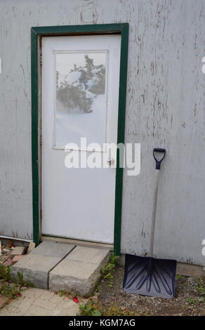 picture of an old shed with a snow shovel leaning on the wall - getting ready for bad weather and winter snow Stock Photo