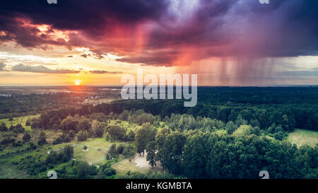 Rain pouring down from a dark heavy clouds on one side of the sky while setting sun is shining on the other side Stock Photo