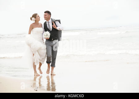 Happy bride and groom walking barefoot on the beach by the sea Stock Photo