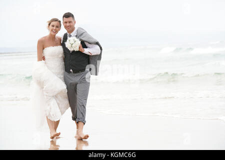 Happy bride and groom walking barefoot on the beach by the sea Stock Photo