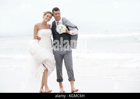 Happy bride and groom walking barefoot on the beach by the sea Stock Photo