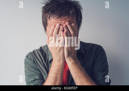 Disappointed man crying with head in hands. Sad and lonely adult male hiding tears. Stock Photo