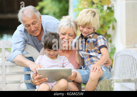Happy grandparents playing game on tablet with kids Stock Photo