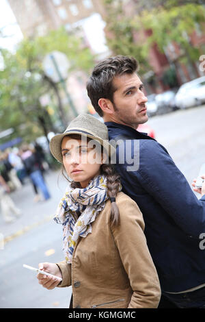 Couple standing back to back in street, using smartphone Stock Photo