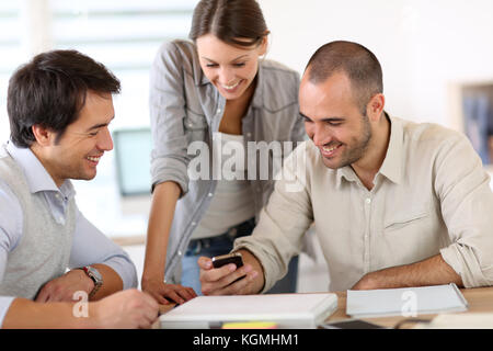 People in office laughing at reading text on smartphone Stock Photo
