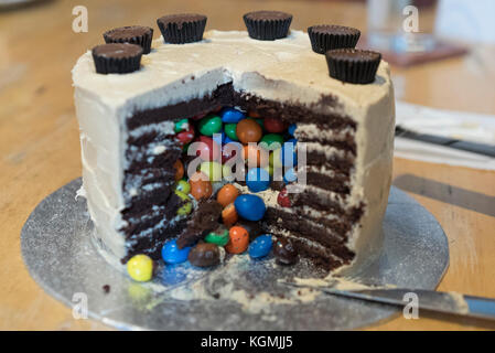 Ornate fancy birthday cake comprising chocolate sponge with peanut icing and enclosing peanut M&M candies inside and Reeses Peanut Cups on top Stock Photo