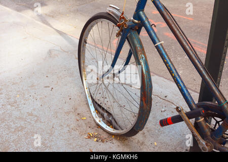 Broken front wheel with loose tyre on an abandoned rusty bicycle, locked to a metal pole. Stock Photo