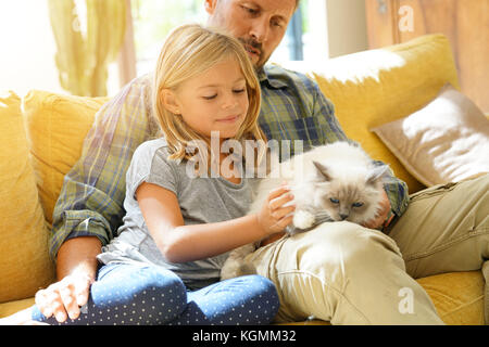 Daddy with little girl petting cat sitting on sofa Stock Photo