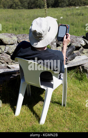 A retired man relaxing on holiday and reading a book on an Amazon Kindle Stock Photo