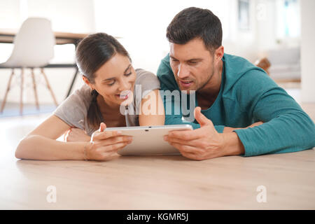 Couple connected on digital tablet, laying on floor Stock Photo