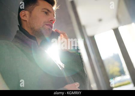 Businessman leaning on wall talking on phone Stock Photo