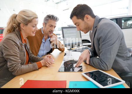 Salesman in car dealership and couple looking at catalogue Stock Photo