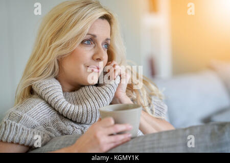 Middle-aged blond woman drinking tea in sofa Stock Photo