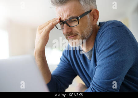 Man at home having a headache in front of laptop Stock Photo