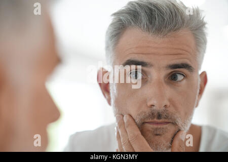 Middle-aged man applying cosmetic on his face, mirror view Stock Photo